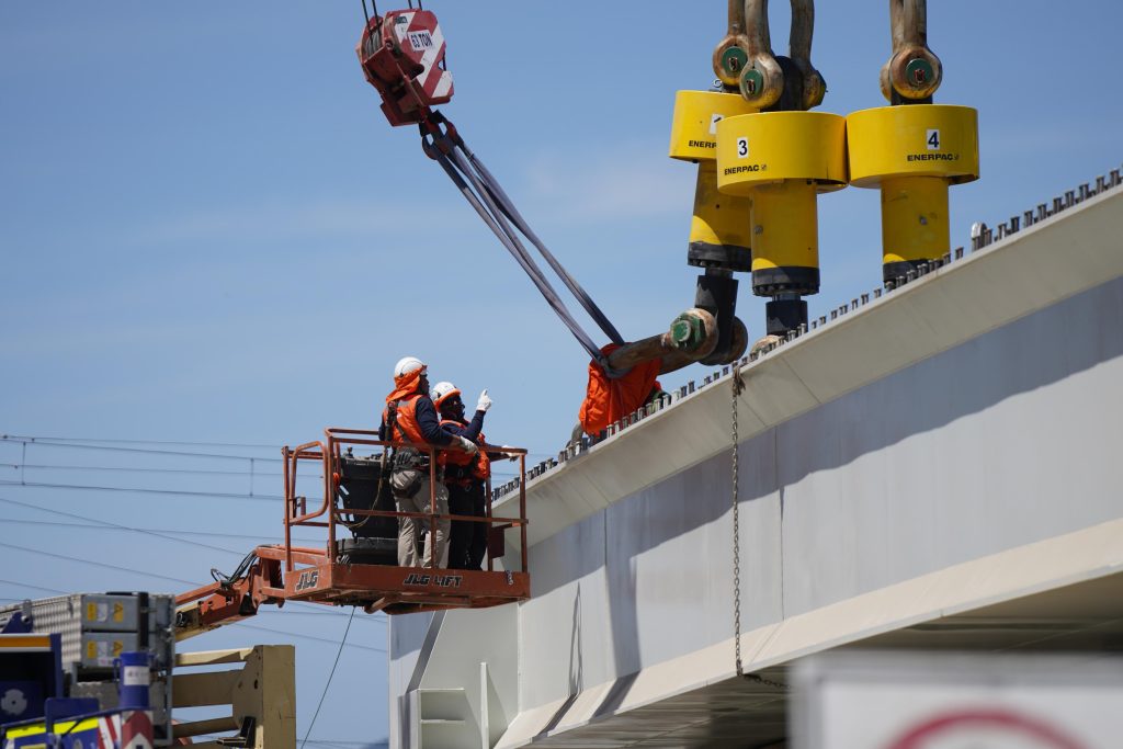 Ironworkers guiding synch hoists on an overpass project.